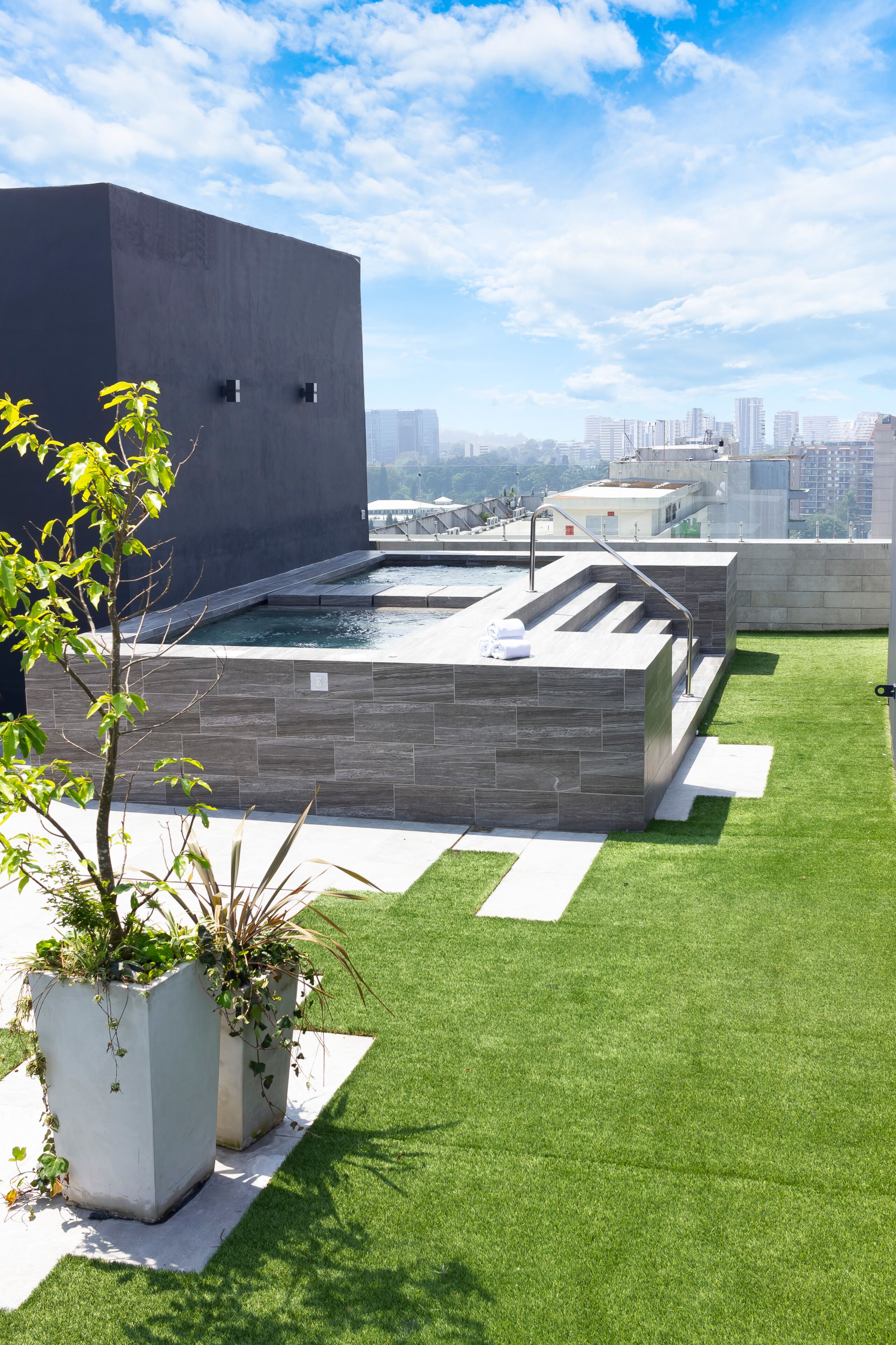 A rooftop pool with a modern design, surrounded by artificial grass and potted plants.