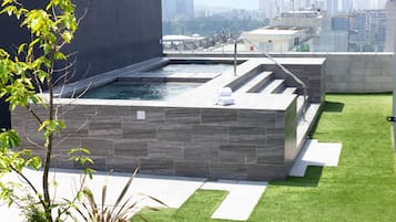 A rooftop pool with a modern design, surrounded by artificial grass and potted plants.