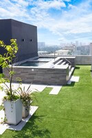 Ein Pool auf dem Dach mit modernem Design, umgeben von Kunstgräsern und Topfpflanzen.