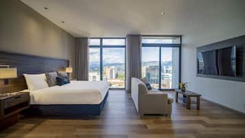 A modern hotel room with a large bed, a sofa, a TV, and a city view.