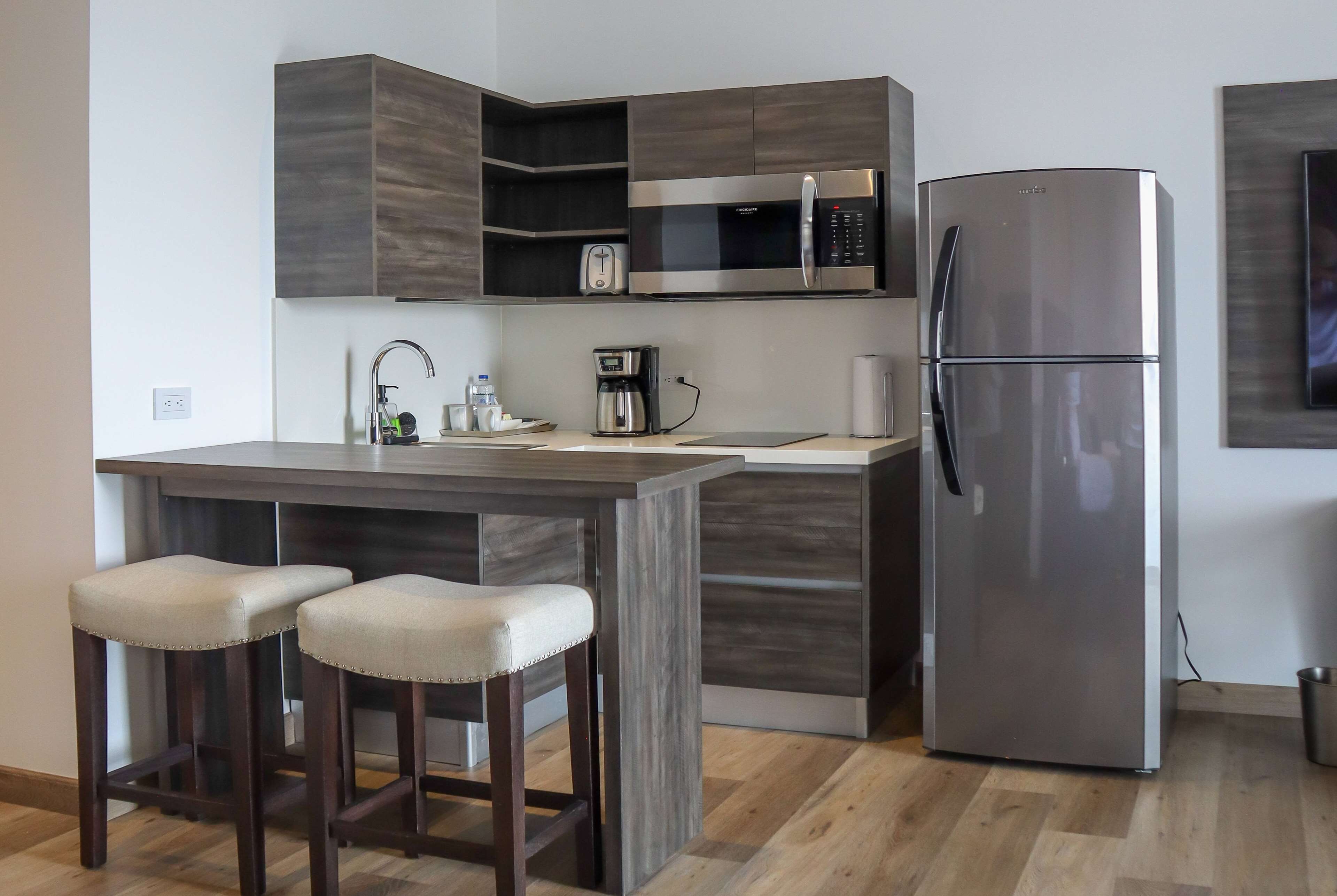 A modern kitchen with a built-in microwave, a stainless steel refrigerator, and a bar area with stools.