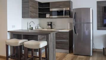A modern kitchen with a built-in microwave, a stainless steel refrigerator, and a bar area with stools.
