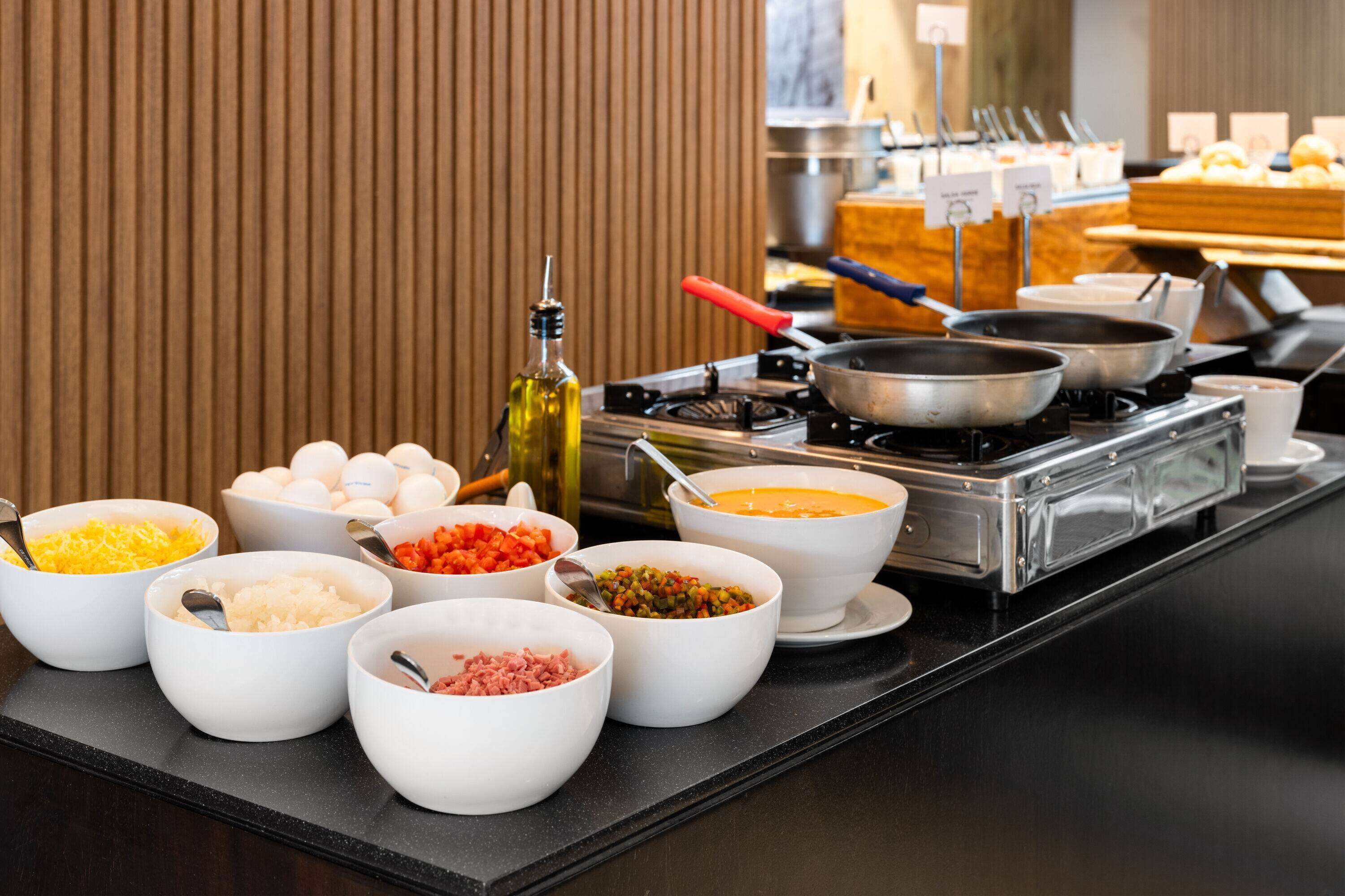 Una barra de buffet con diversos alimentos en recipientes y utensilios de cocina sobre una encimera.
