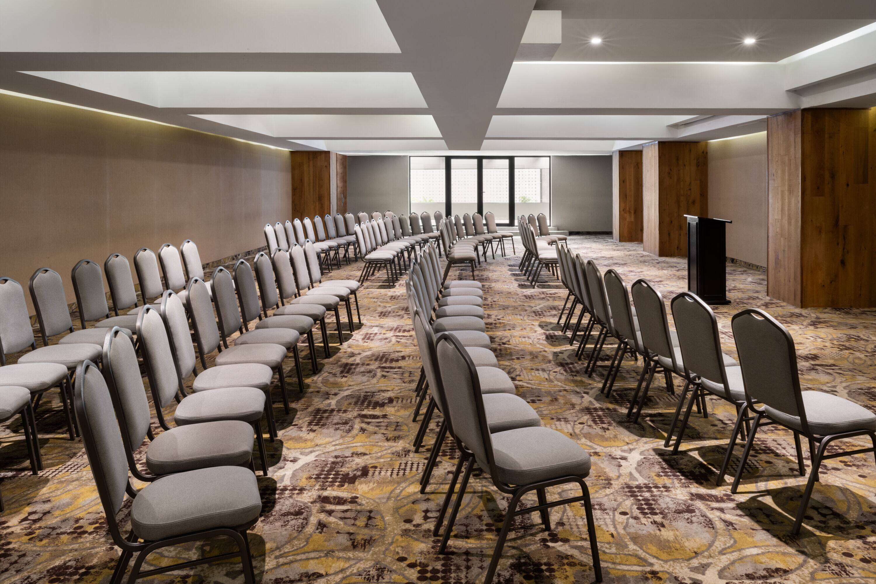 A conference room with rows of chairs, a carpeted floor, and a large window.