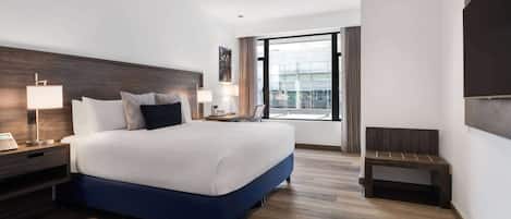Una habitación de hotel moderna con una cama grande, lámparas de noche, una mesita de noche, un pequeño banco y un ventanal con vistas.
