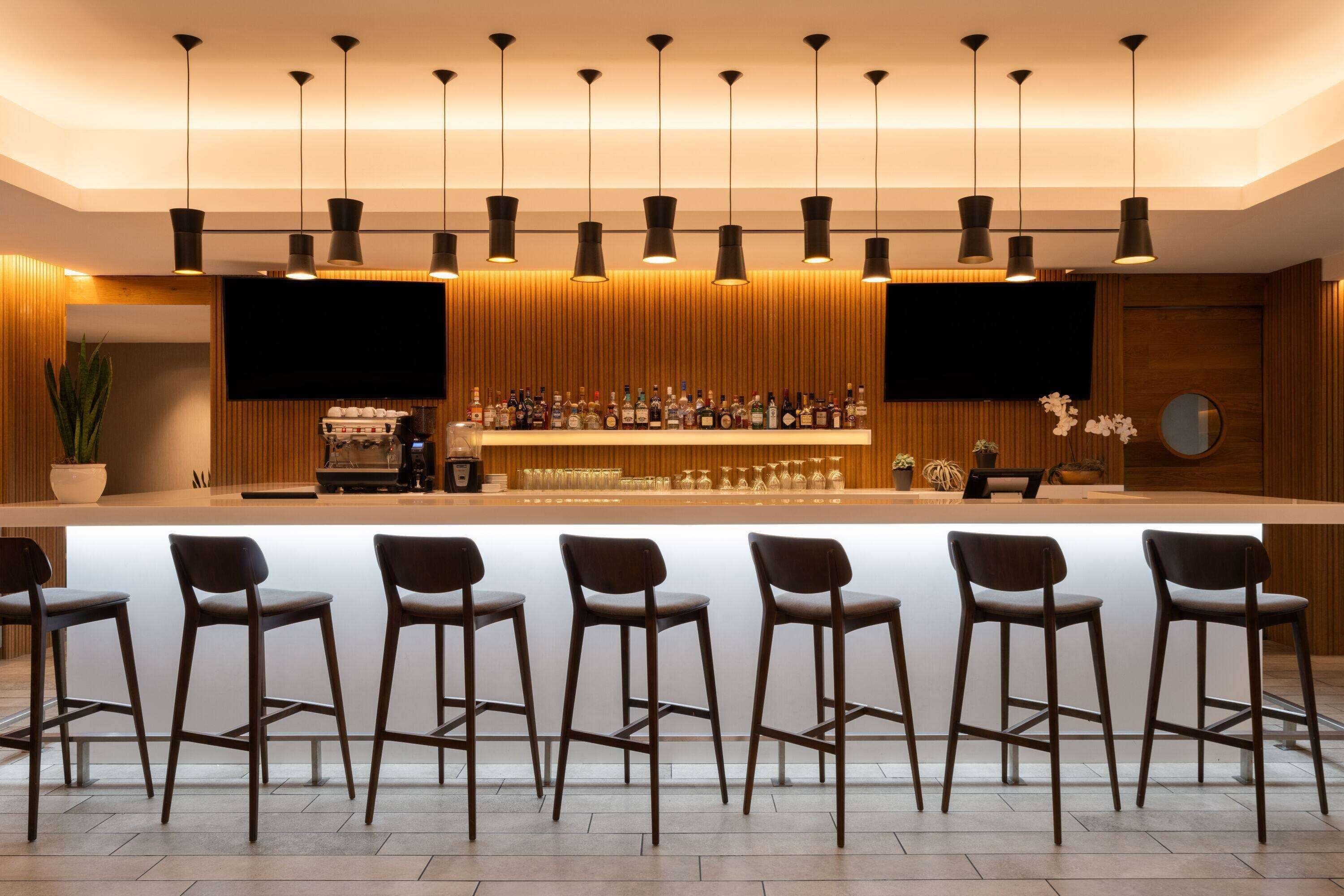 A bar area with a long counter, multiple bar stools, and a television screen.