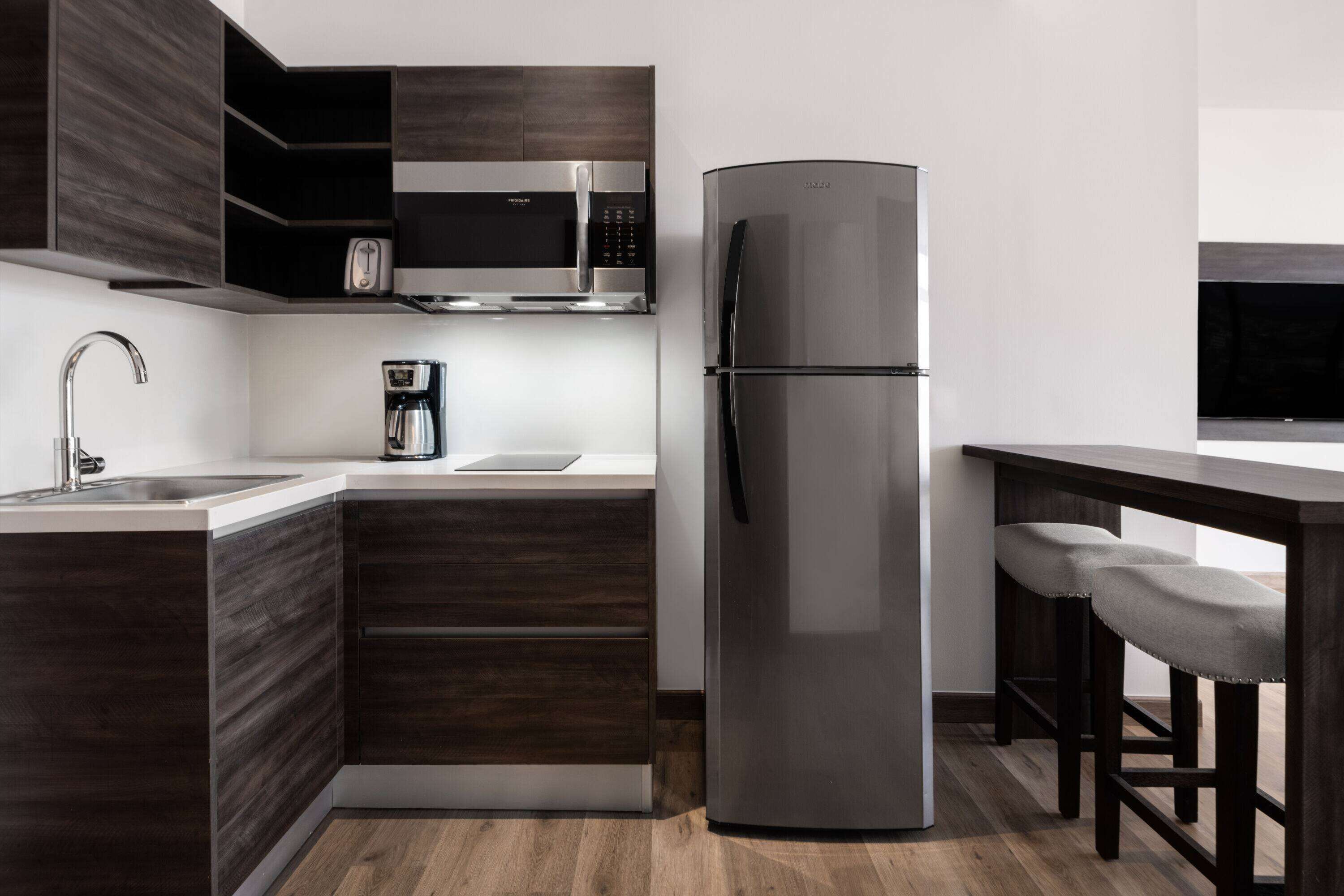 A modern kitchen with dark wood cabinetry, stainless steel appliances, and a built-in coffee maker.
