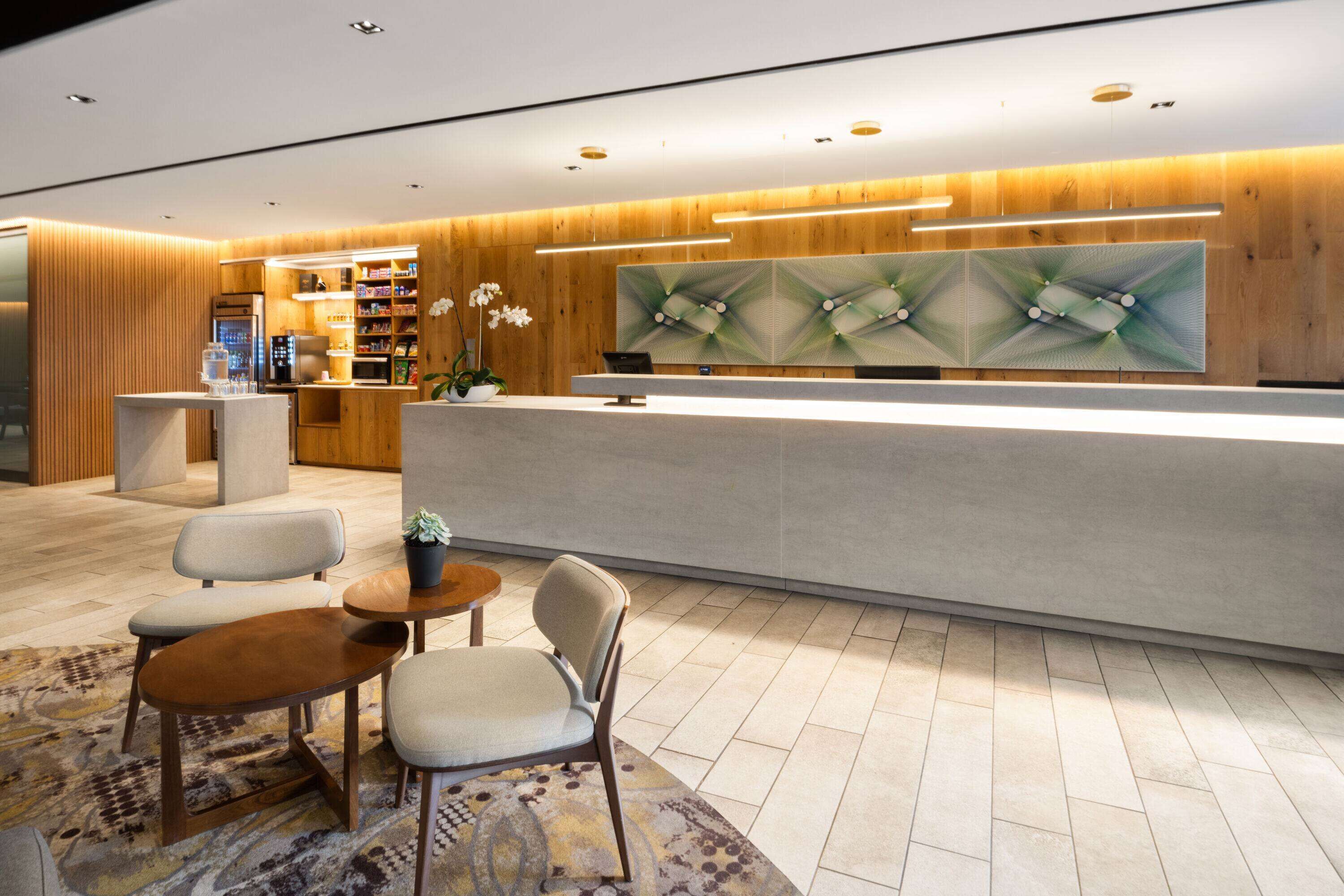 A modern reception area with a wooden reception desk, a seating area with two chairs and a small table, and a decorative wall piece.
