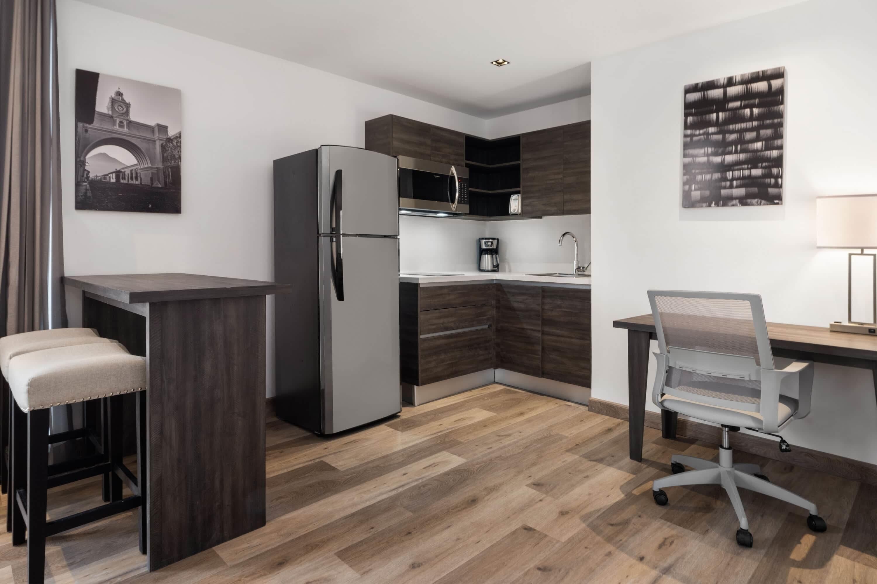 A modern kitchen with a refrigerator, coffee maker, and a dining area with stools.
