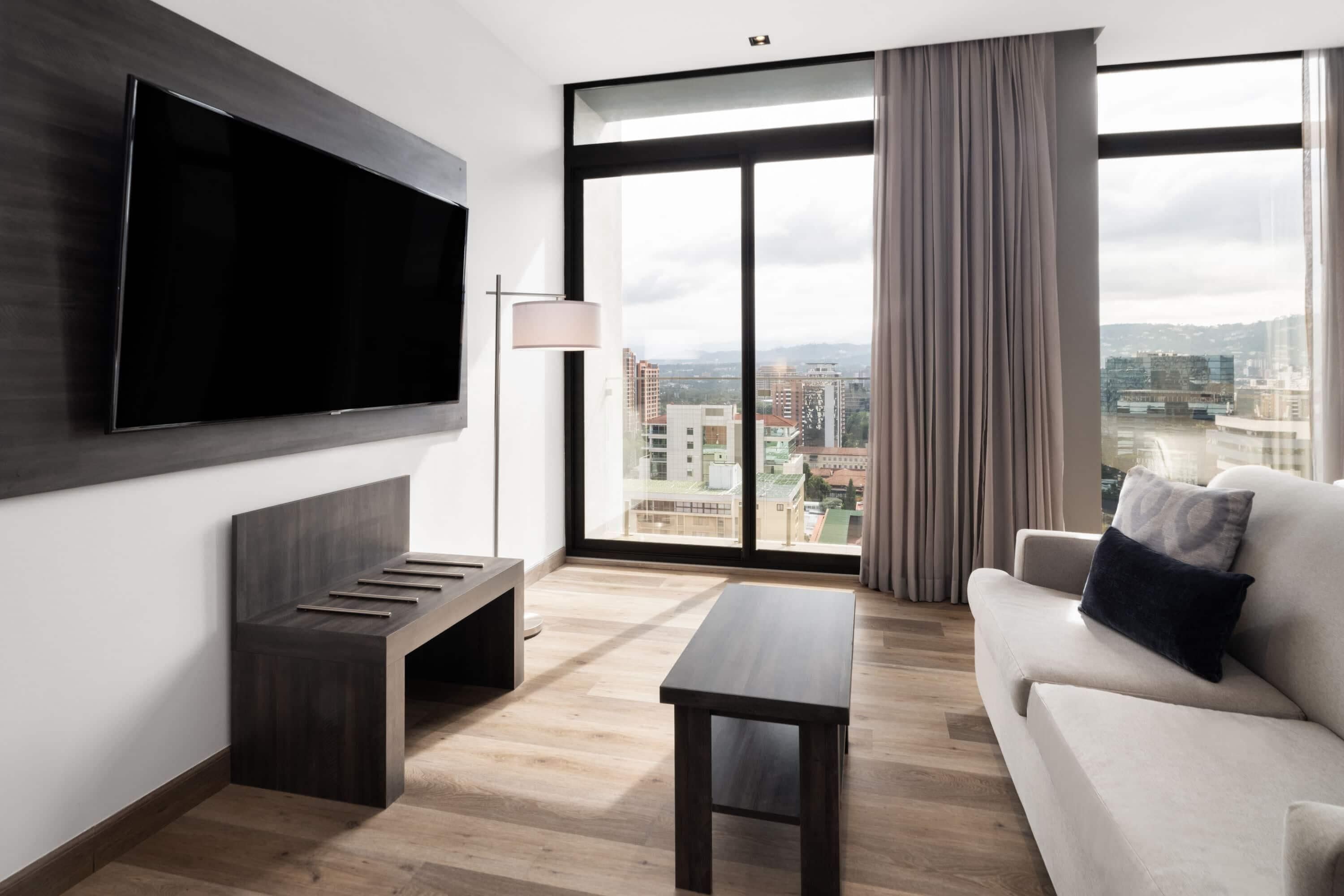Un salon moderne avec une grande télévision, un canapé, une table basse et un banc.