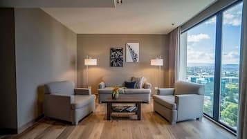 Una sala de estar moderna con un sofá, dos sillones, una mesa de centro y dos lámparas de pie. Hay dos cuadros enmarcados en la pared y un ventanal con vistas a la ciudad.