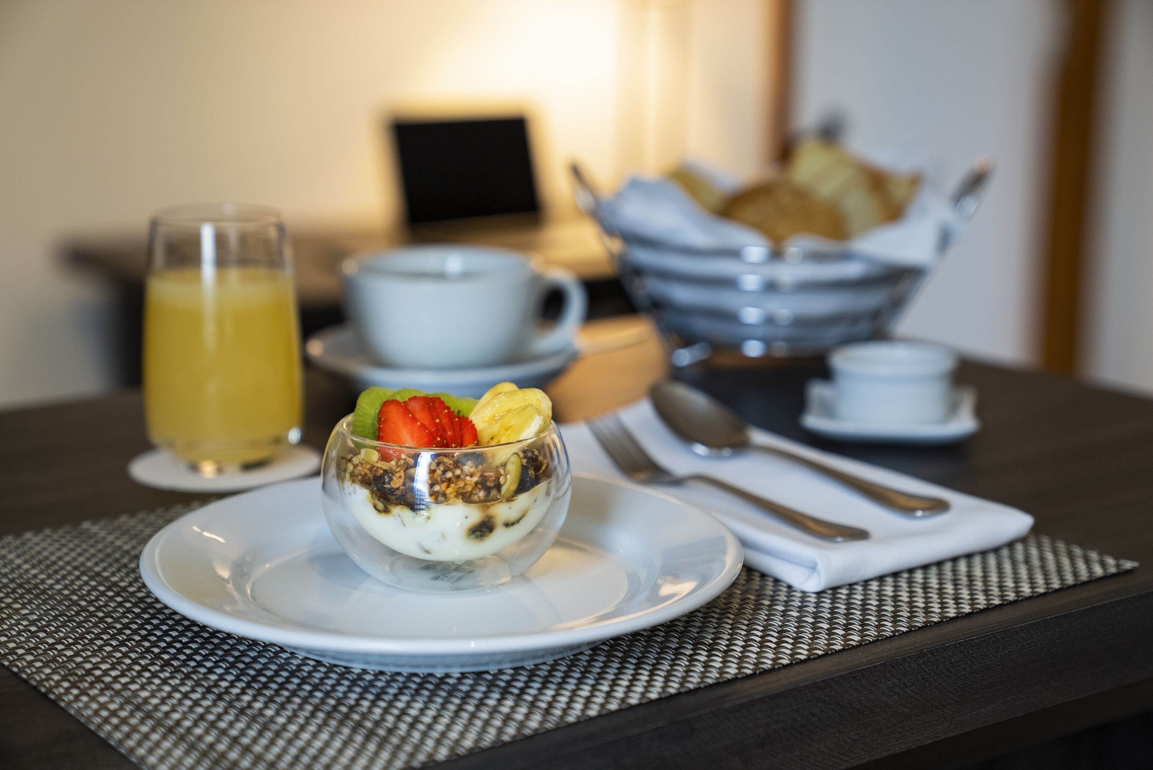 Ein Frühstückstisch mit Orangensaft, Joghurt mit Früchten und einer Tasse Kaffee.