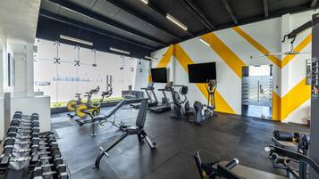 Un gimnasio con diversos equipos de ejercicio, como cintas de correr, bicicletas estáticas y mancuernas.