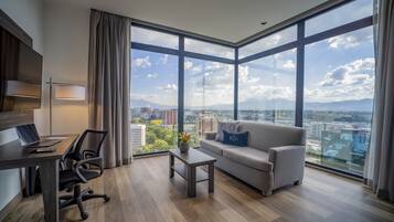 A modern living room with a large window, a sofa, a coffee table, and a desk with a laptop.