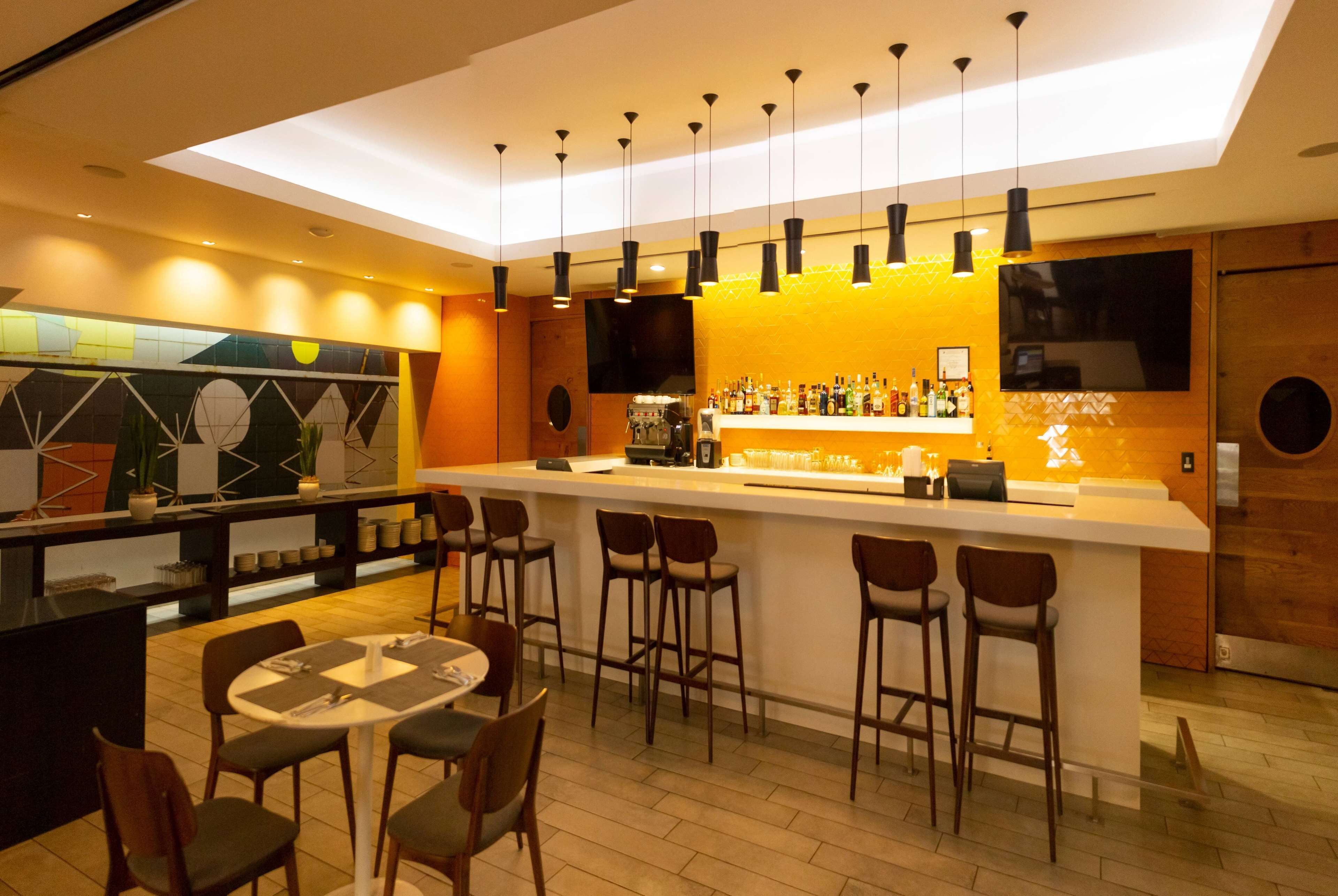 Een moderne bar met een lange toonbank, verschillende krukken en een zithoek met tafels en stoelen.