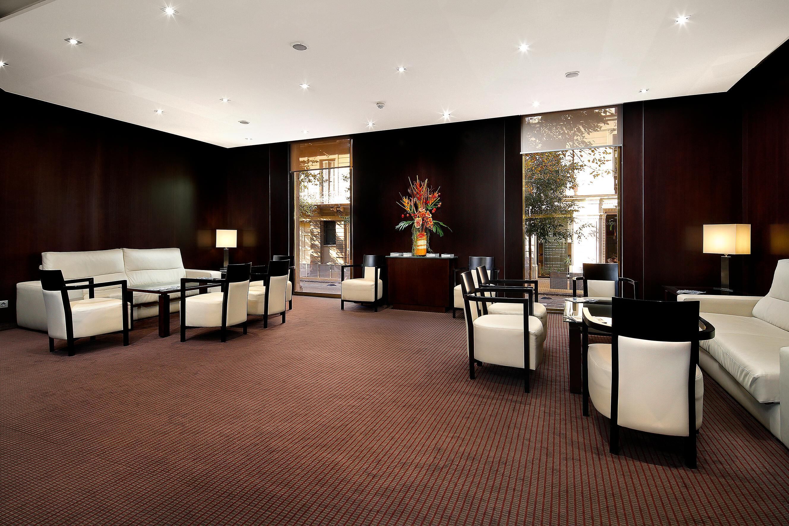 A spacious hotel lobby with a red carpet, white sofas, and black chairs.