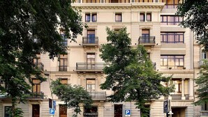 Un hôtel à plusieurs étages doté de balcons, d’un panneau indiquant un parking et situé dans une rue bordée d’arbres.