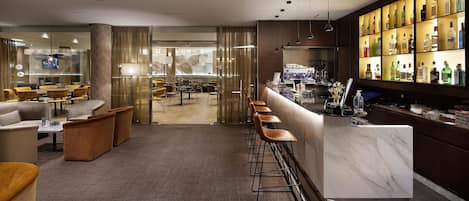 Zona de bar moderna con mostrador de mármol, taburetes y una exhibición de botellas de licores.