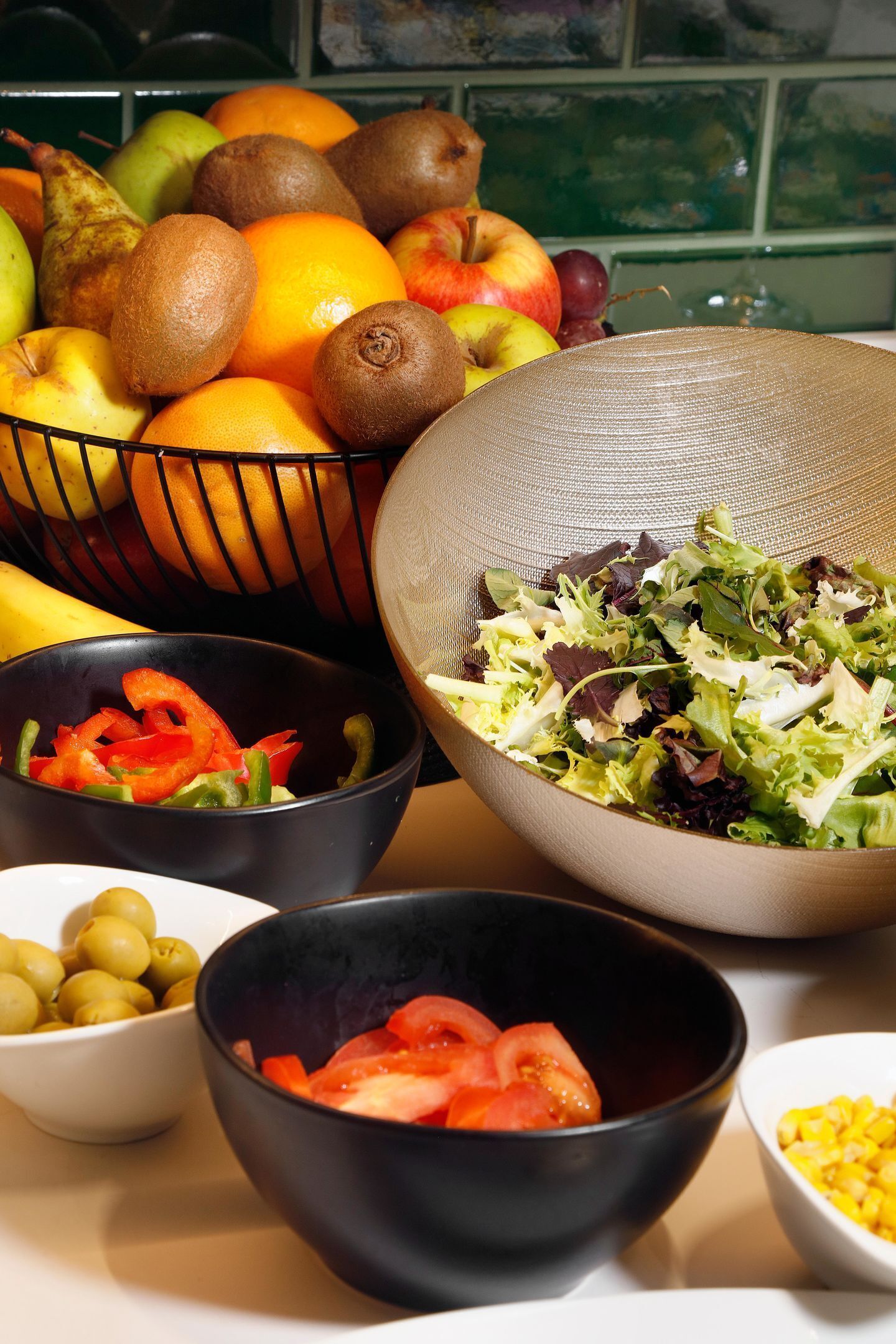 Uma bancada de cozinha com diversas frutas e legumes, incluindo kiwis, laranjas, maçãs e tomates.