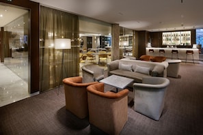 A modern hotel lobby with a bar area, seating arrangements, and a view of the cityscape.
