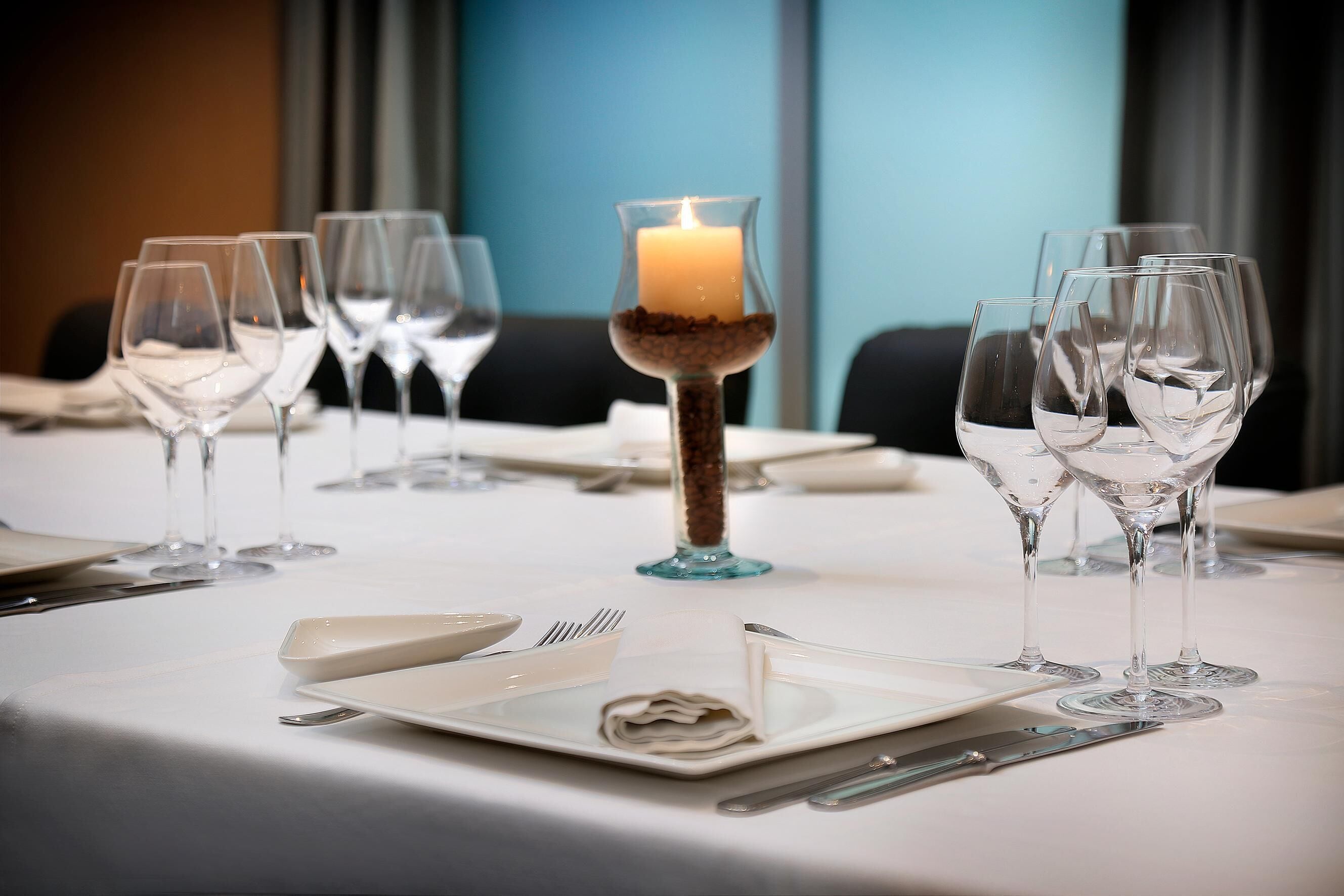 Mesa posta para refeição com taças de vinho, vela e talheres.