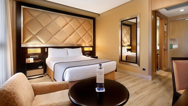 Une chambre d’hôtel avec un grand lit, une table de chevet, une chaise, une table ronde et un miroir.