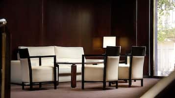 Una habitación con pared de madera oscura, un sofá blanco, una mesa de comedor con cuatro sillas y una lámpara.