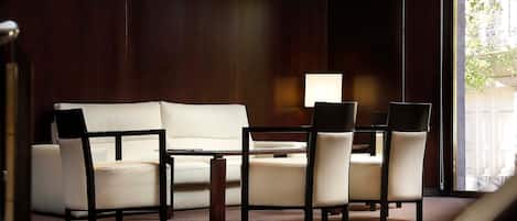 Una habitación con pared de madera oscura, un sofá blanco, una mesa de comedor con cuatro sillas y una lámpara.