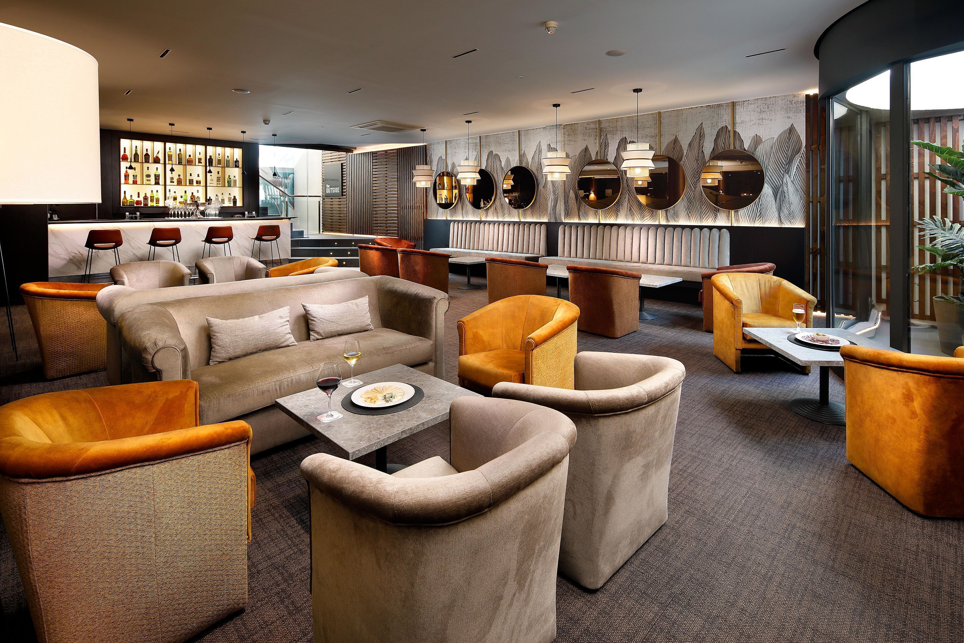 A modern lounge area with comfortable seating, a bar with a variety of bottles, and a large window offering a view.