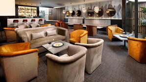 Un espace lounge moderne doté de sièges confortables, d’un bar proposant un large choix de boissons et d’une grande fenêtre offrant une vue panoramique.