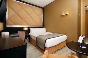 Une chambre d’hôtel avec un grand lit, un bureau, une chaise, une table de chevet et un téléviseur fixé au mur.