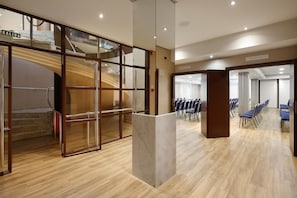 A modern hotel lobby with a staircase, a reception desk, and rows of blue chairs.