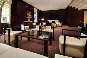 A modern lobby with a glass coffee table, leather chairs, a sofa, and a large vase with flowers. - HCC St. Moritz (Barcelona)