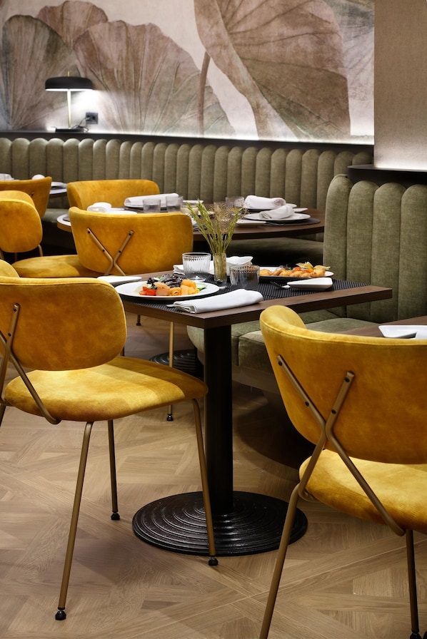 A restaurant with yellow upholstered chairs, a round table with a black base, and a wall mural.