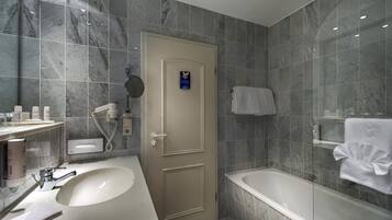 Um banheiro moderno com parede revestida em mármore, pia branca, banheira e porta com porta-toalhas.