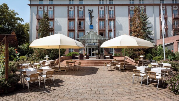 A hotel with outdoor seating, a central entrance, and a large building facade.