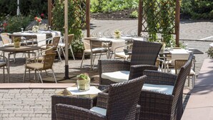 An outdoor patio with wicker furniture, white tablecloths, and umbrellas. - Radisson Blu Hotel, Halle-Merseburg (Merseburg)
