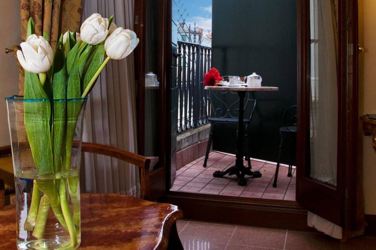 Une pièce comprenant une table à manger, des chaises, un vase avec des fleurs et donnant sur le balcon extérieur.
