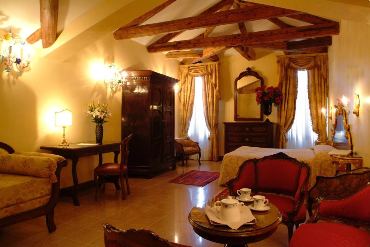 Une chambre traditionnelle comprenant un lit, deux fauteuils, une table avec un service à thé, une armoire en bois et un lustre.