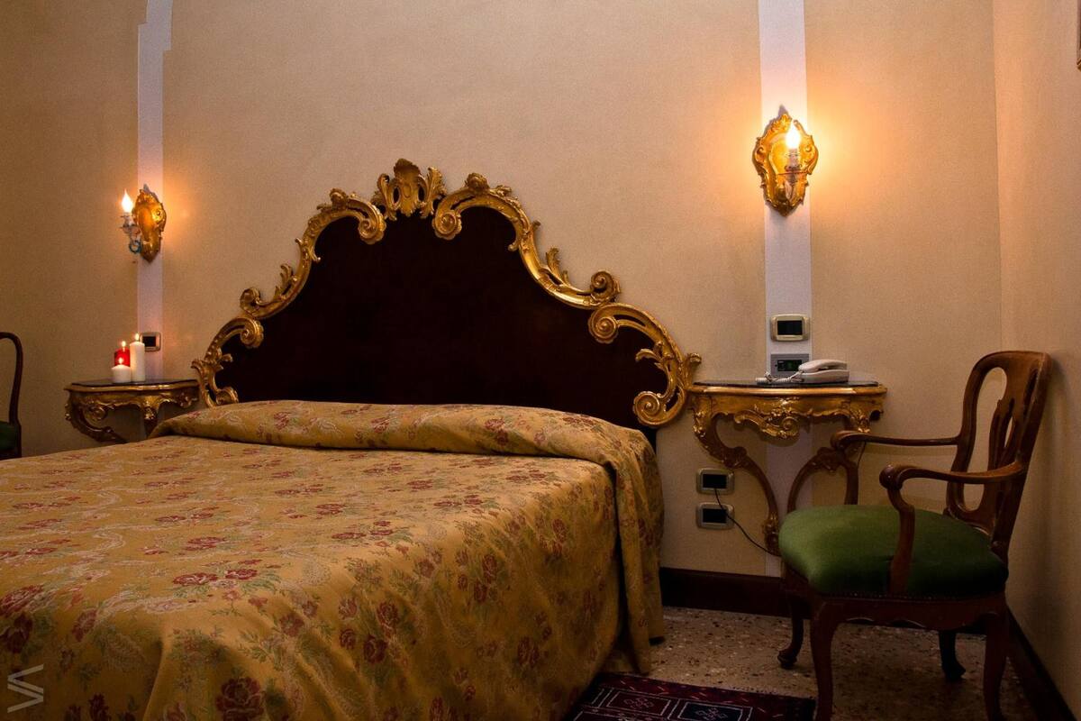 Une chambre d’hôtel avec un grand lit, une chaise en bois, deux tables de chevet avec des lampes et un luminaire fixé au mur.
