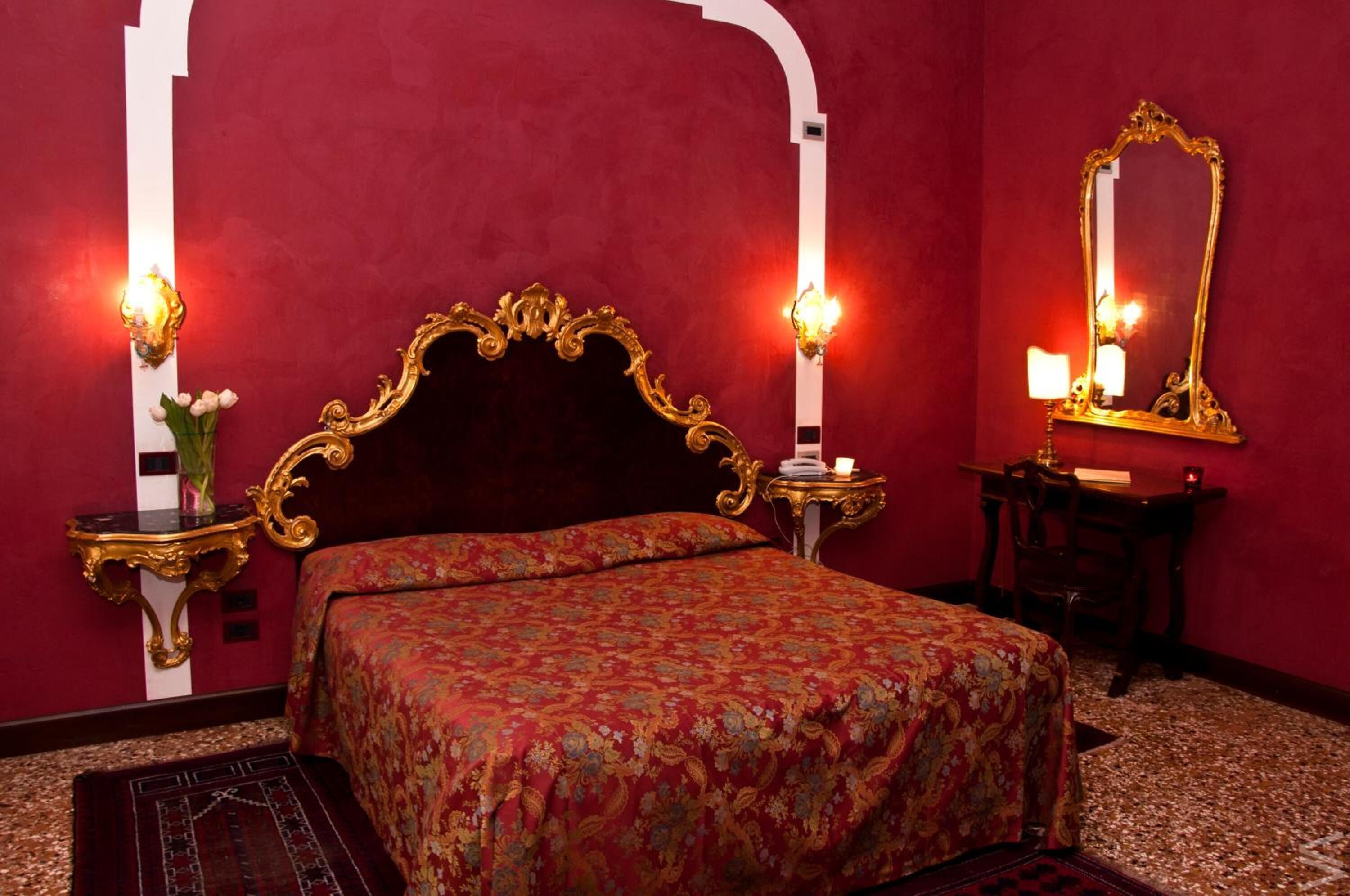A room with a large bed, ornate gold-framed headboard, and two wall-mounted sconces.