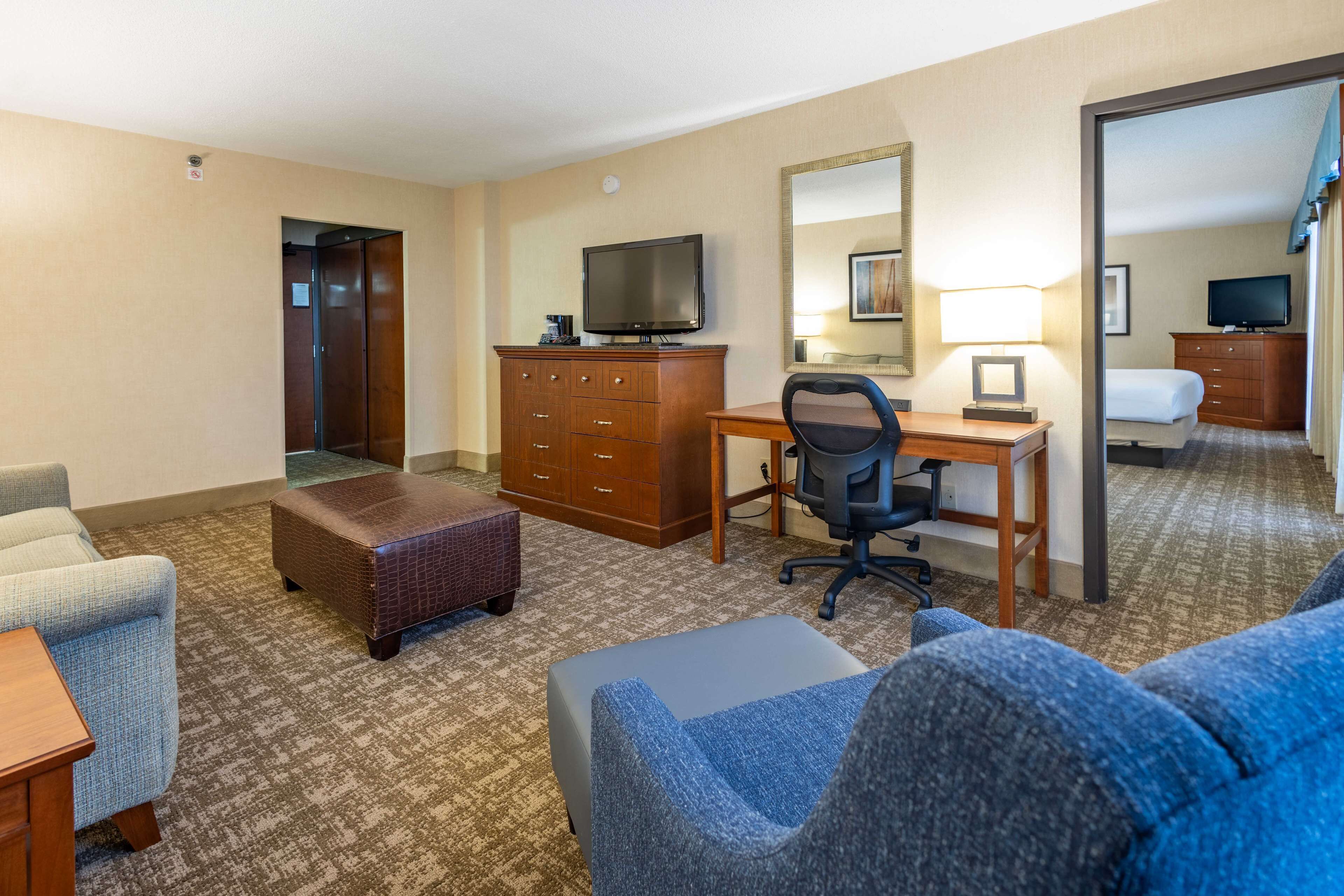 A hotel room with a sofa, a desk with a computer, a television, a dresser, and a mirror.