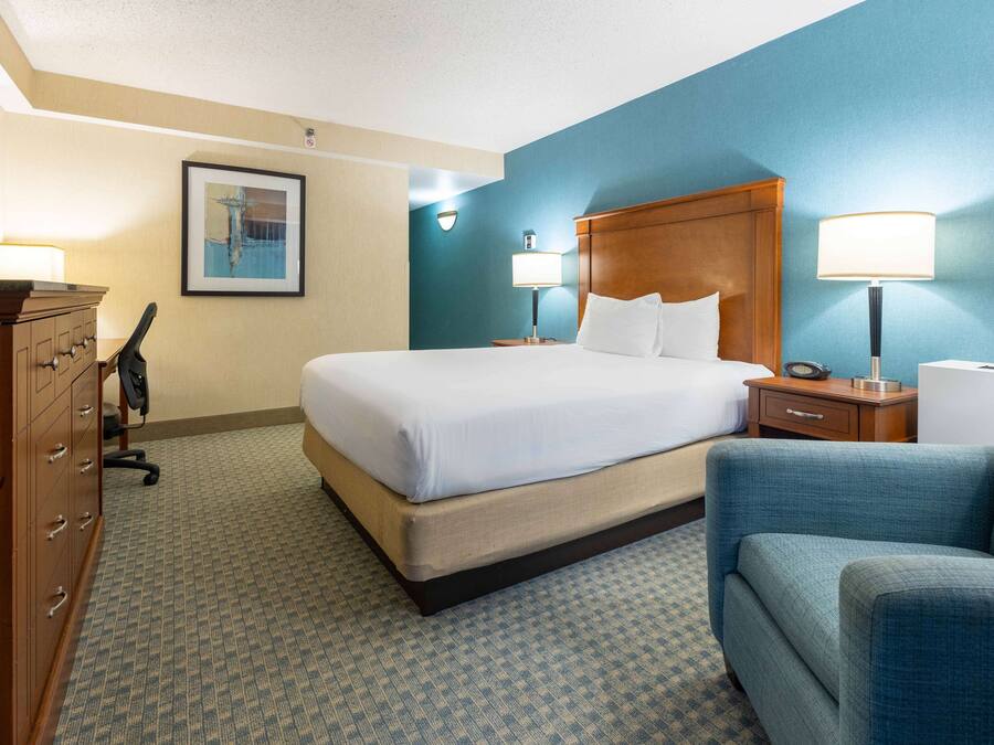 Ein Hotelzimmer mit einem großen Bett, einem hölzernen Kopfteil, einem Schreibtisch mit Lampe, einem Sessel und einem Schminktisch.