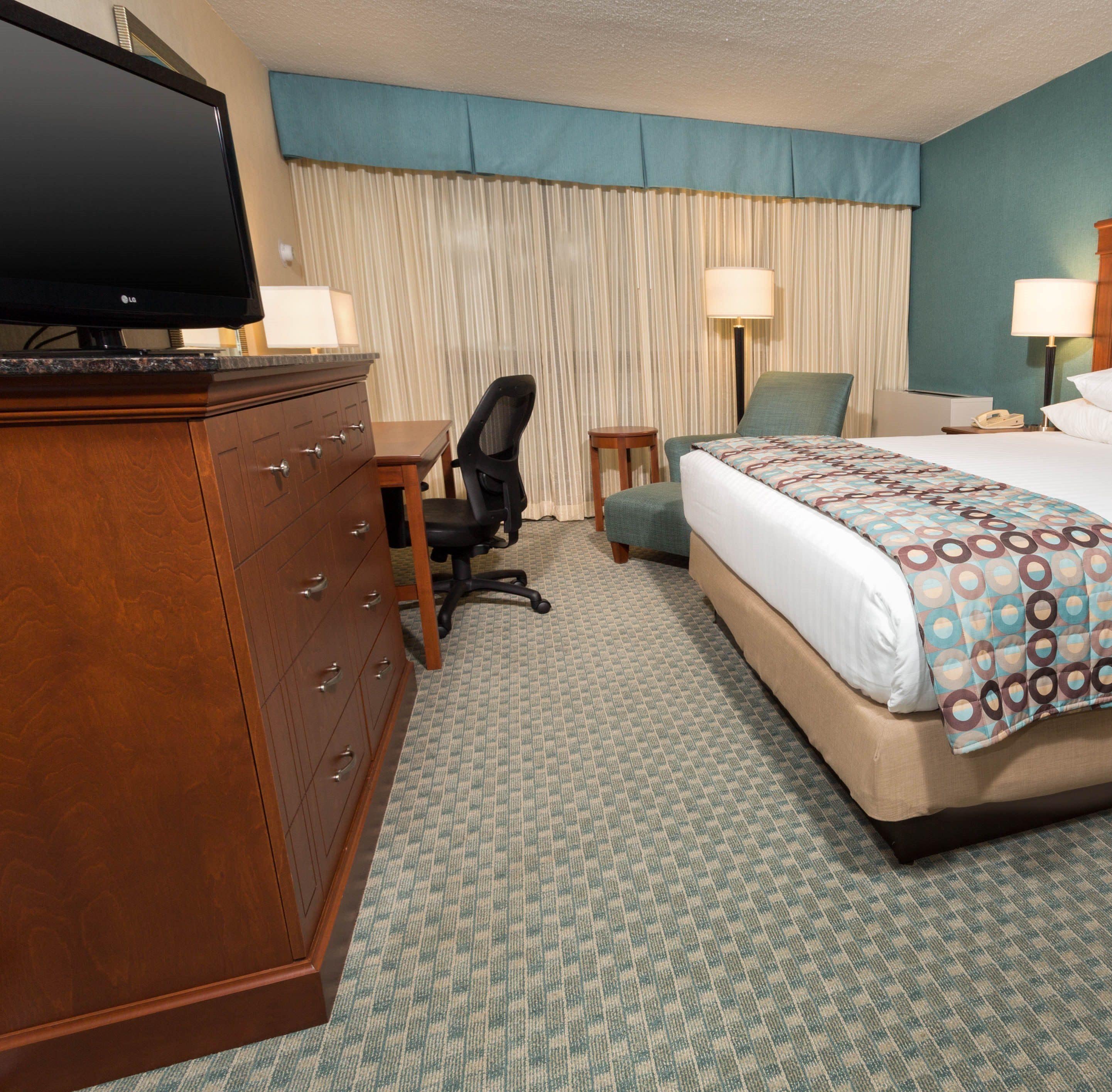 A hotel room with a bed, a desk, a chair, a dresser, and a television.
