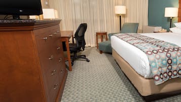 A hotel room with a bed, a desk, a chair, a dresser, and a television.