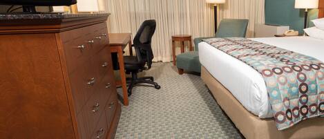 A hotel room with a bed, a desk, a chair, a dresser, and a television.