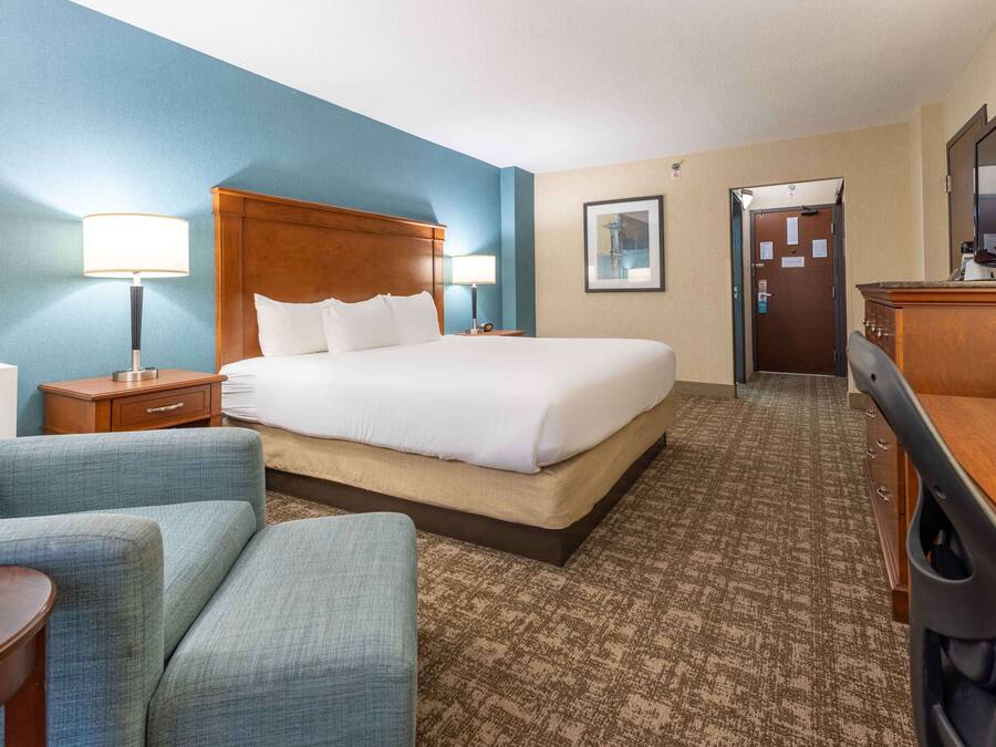 Quarto de hotel com uma cama grande, duas mesas de cabeceira com luminárias, uma escrivaninha e um armário.
