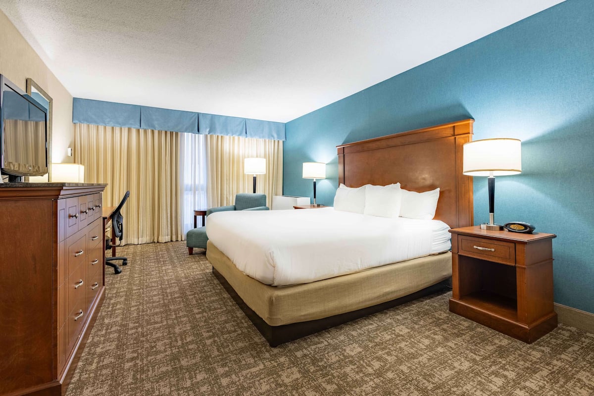 Ein Hotelzimmer mit einem großen Bett, zwei Nachttischlampen, einem hölzernen Nachttisch, einem Schreibtisch mit Stuhl und einer Kommode.