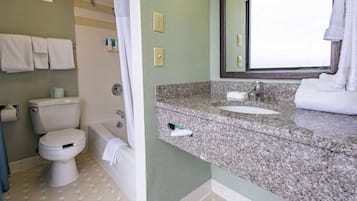 A bathroom with a toilet, bathtub, and granite countertop sink.