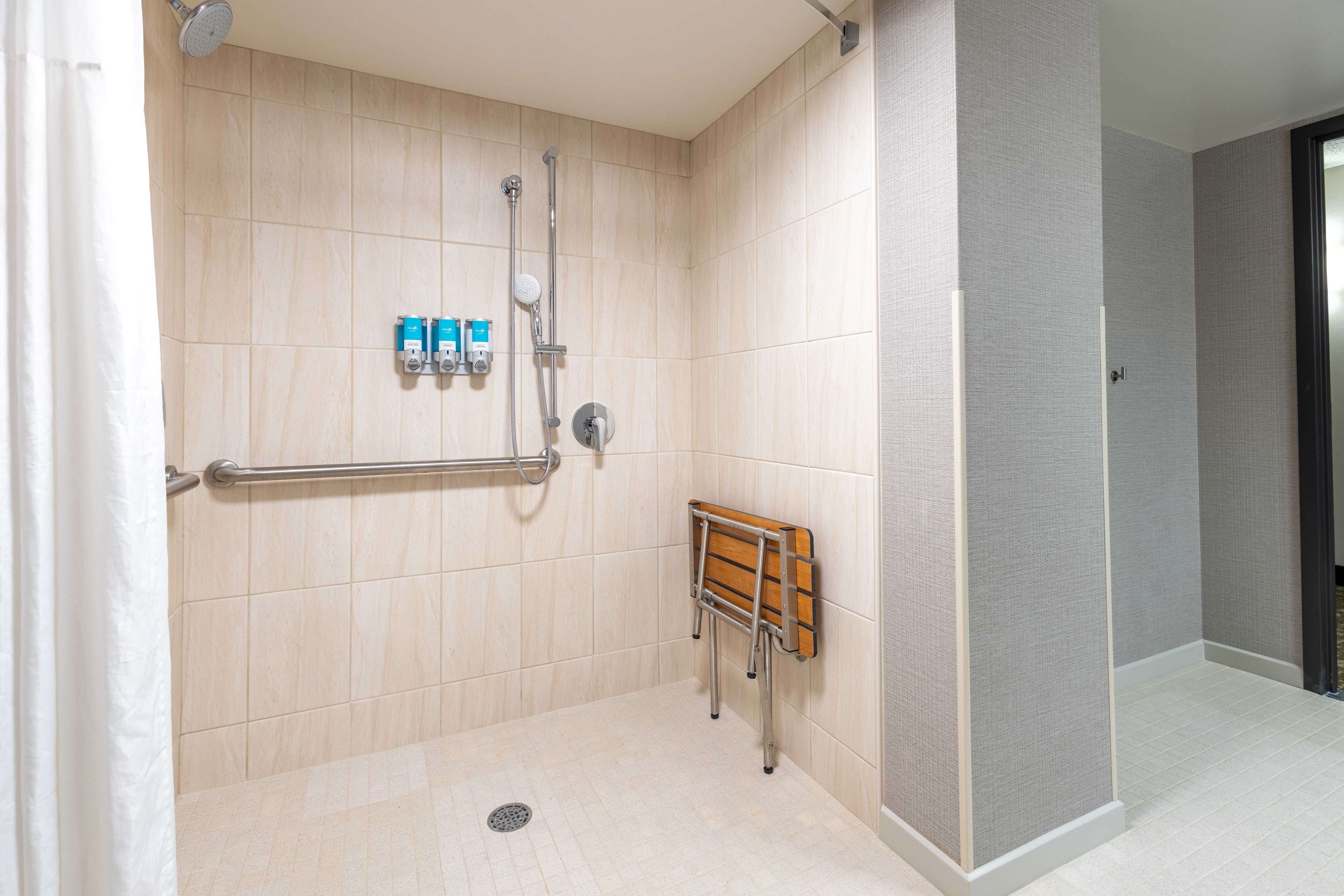 A shower area with a grab bar, a wooden bench, and toiletries on the wall.